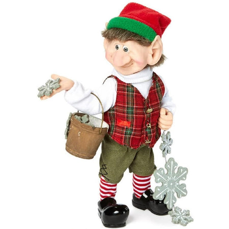 Standing elf figure with red and white stripped socks, red hat with green trim, plaid vest over white turtleneck and green shorts. He holds a bucket on his arm and snowflakes in his hands.