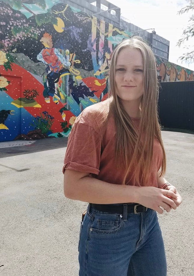 photo of girl with long hair wearing jeans and t-shirt outside in front of a mural