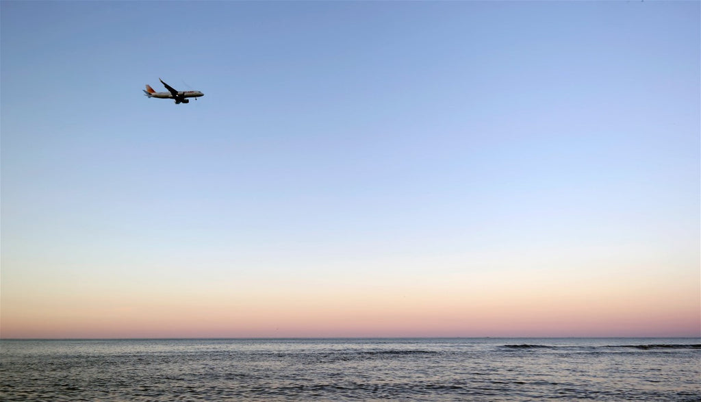 view of airplane flying in distance over a beach at sunset