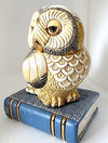 side vie of Owl figure on a blue hardback book figure.  The owl is off white with black feathers and gold accent.