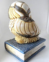 back view of Owl figure on a blue hardback book figure.  The owl is off white with black feathers and gold accent.