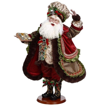 Santa wearing a vest with candy buttons, a red and green coat trimmed in brown fur and a matching hat, he's holding a tray of chocolate candy.