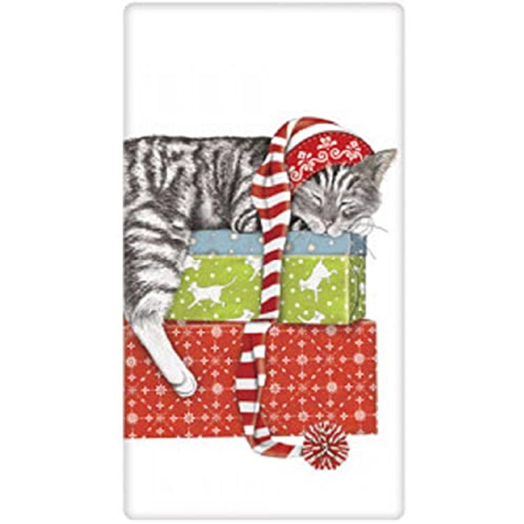 White kitchen towel with a sleeping cat wearing a very long stocking cap sleeping on top of 2 gifts