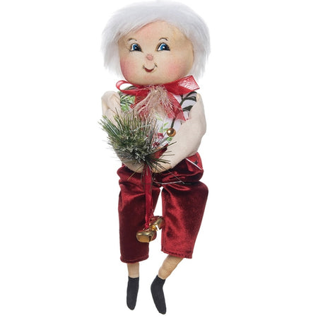 Doll figure with white hair wearing red bow and pants.  Holding  a red ribbon with jingle bell and pine swag. bo