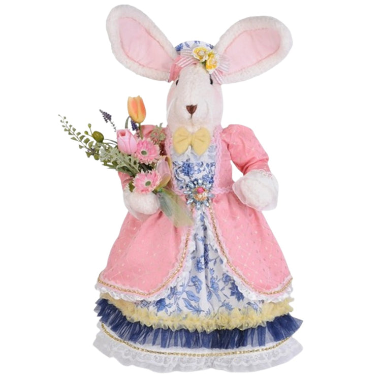 Standing girl bunny figurine. She wears a long dress in white and blue floral print with a pink jacked. She carries pink and yellow tulips and pink flowers. Bunny ears are pink inside and she wears a matching blue floral hat.