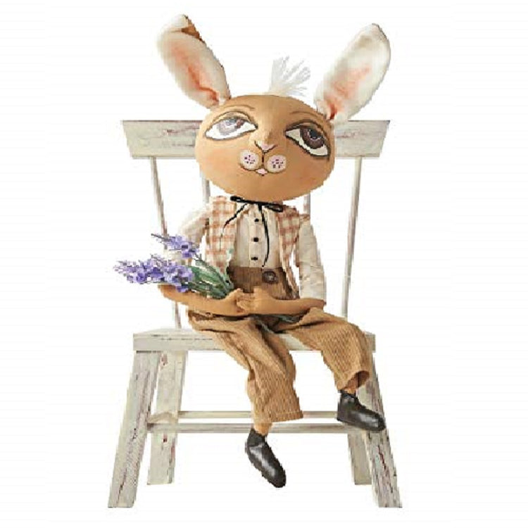 Rabbit figure sitting in a chair. He has large white with pink ears, wearsh a tan and white plaid vest with white long sleeve shirt and tan pants. Black booties he holds purple flowers.