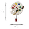 clock in white shaped like a painters pallet with colored paint like numbers and a paint brush.  Pendulum is a red tube of paint.  Lines on side and bottom indicate sizes of 13 inches and 8.5 Inches