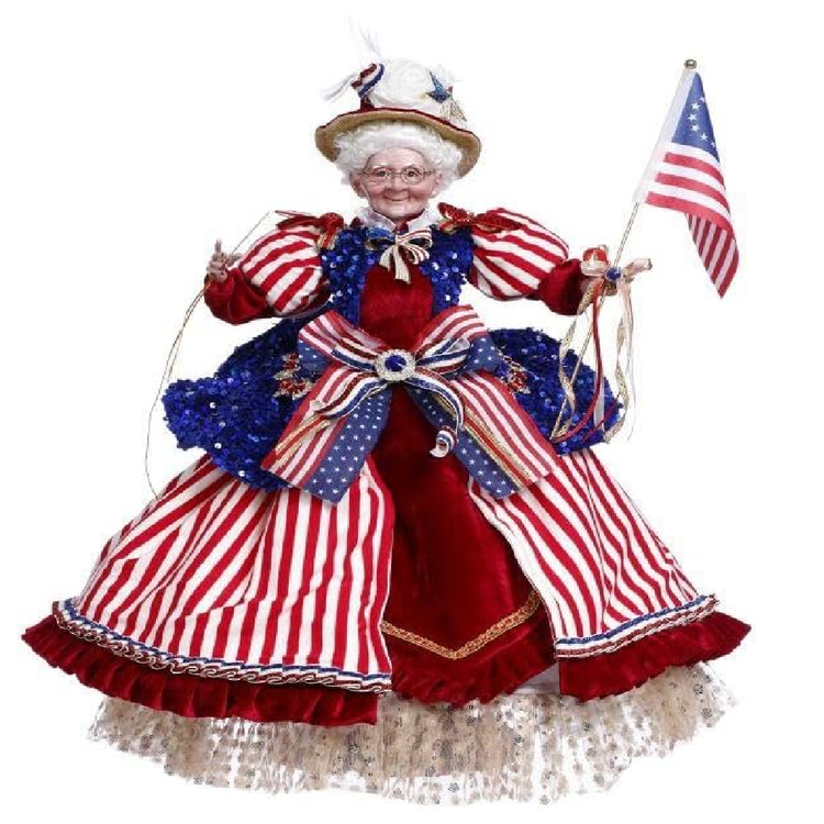 Betsy Ross figurine in a patriotic outfit with an American flag on a white background