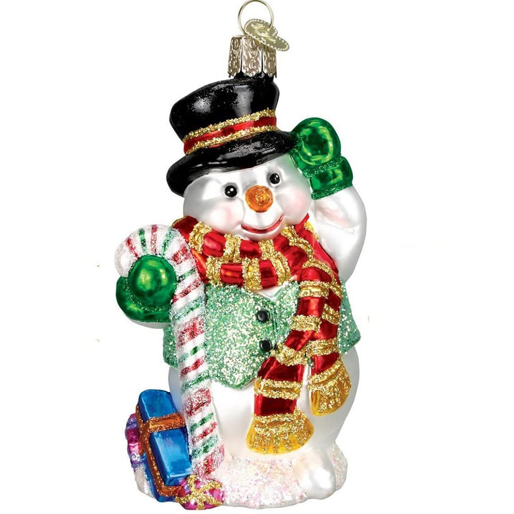 Snowman ornament with black top hat, carror nose and black eyes. He is wearing green mittens, a red and gold scarf and a green vest.  Holding a candy cane and has a blue gift at his feet.