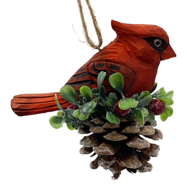 red cardinal carved in wood sitting on a pine cone with holly accent. Twine hanger