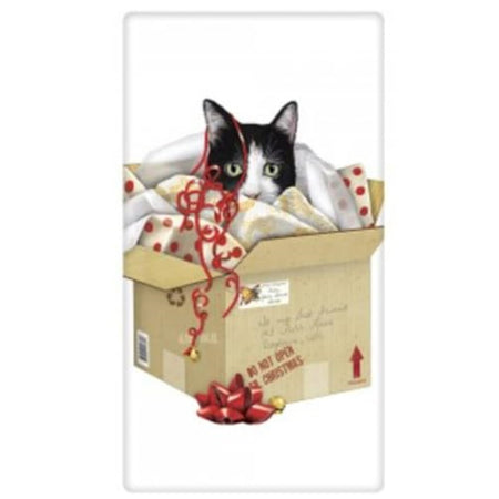 White kitchen towel with a print of a cat inside a brown box from the mail.  The cat is playing in the wrapping paper and ribbon from the box. The cat is black and white