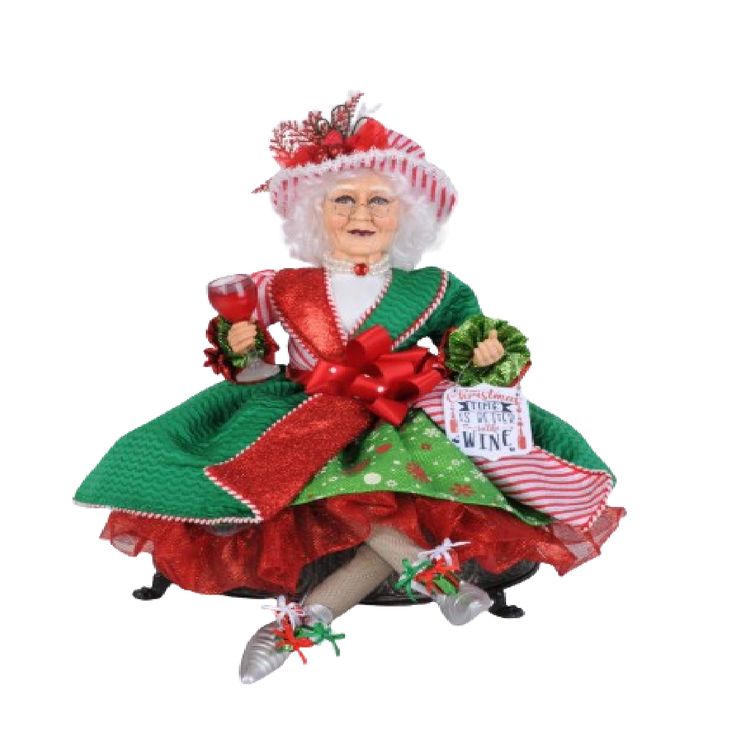 mrs. claus figurine, sitting cross legged wearing green and red outfit and holding a glass of wine.