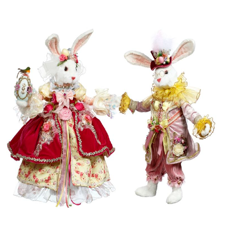 two white fluffy rabbit figurines, one in pink and yellow suit, one in red and yellow gown.