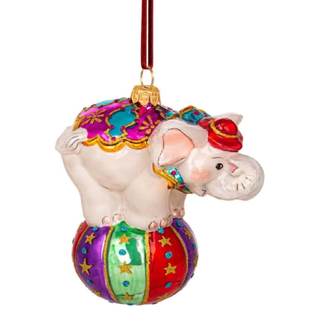 A colorful Christmas ornament shaped like a white elephant standing on a striped ball, with a red hanging ribbon at the top, shown on a plain white background.