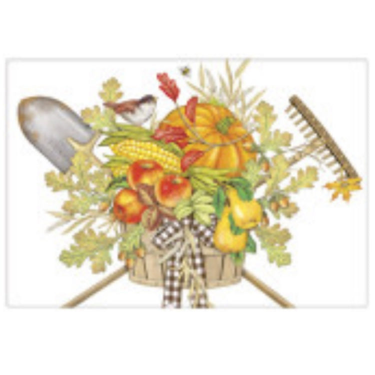 White towel with a tan wood basket with fall leaves, apples a pumkin and pears in it.  There is also a rake and shovel criss crossed behind it.