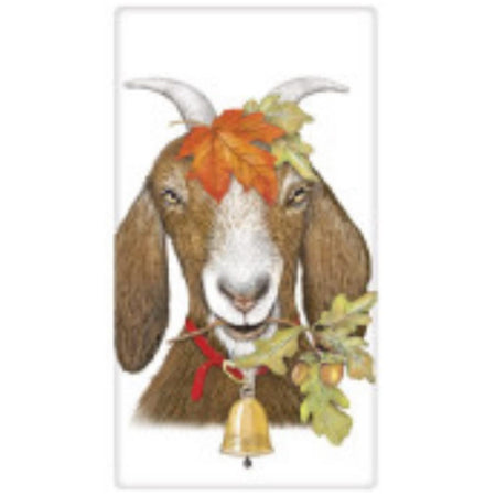 Brown and white goat face view. He has horns, an orange leaf on his head and in his mouth, a bell around his neck.