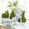 Moss-covered bunny figurines on a table with a floral-patterned cup and white flowers in the background.