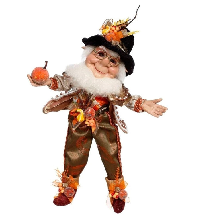 This elf figurine is wearing a brown and orange suit, a black hat and orange shoes, all with squash, pumpkin and ribbon accents.
