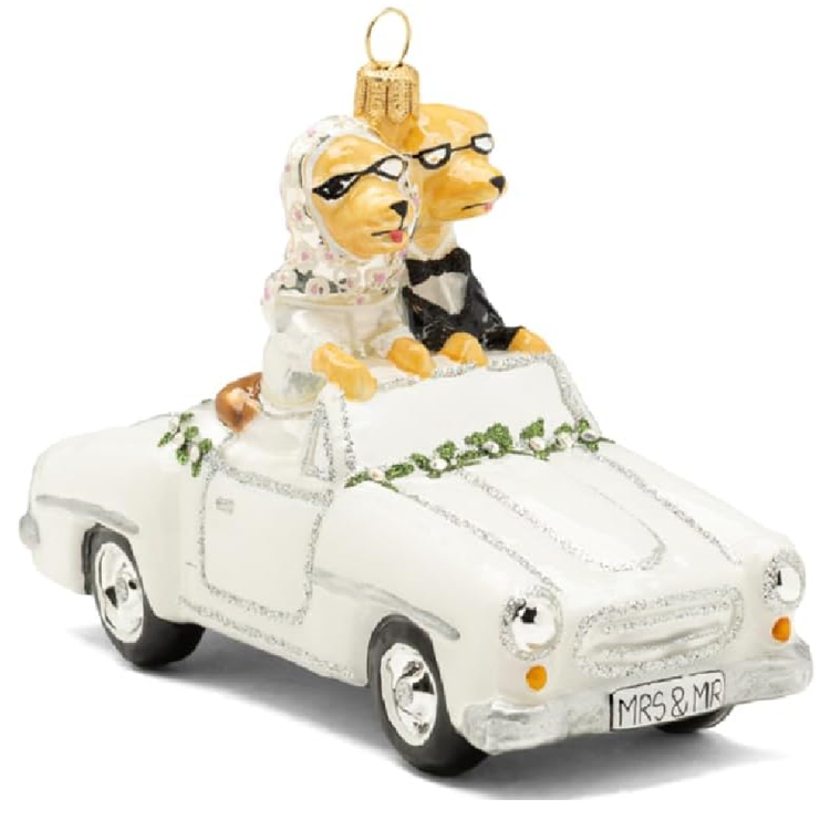 A white Christmas ornament shaped like a vintage convertible car with two dogs dressed as a bride and groom sitting inside. The bride dog wears a white veil and black glasses, and the groom dog wears a black tuxedo.