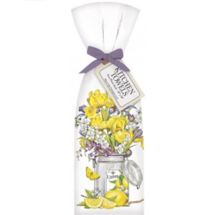 white kitchen towel folded and tied with ribbon.  Print is a clear jar with a sticker that says lemon and shows lemons. The jar has yellow and purple flowers with cut lemons on the table and a yellow butterfly.