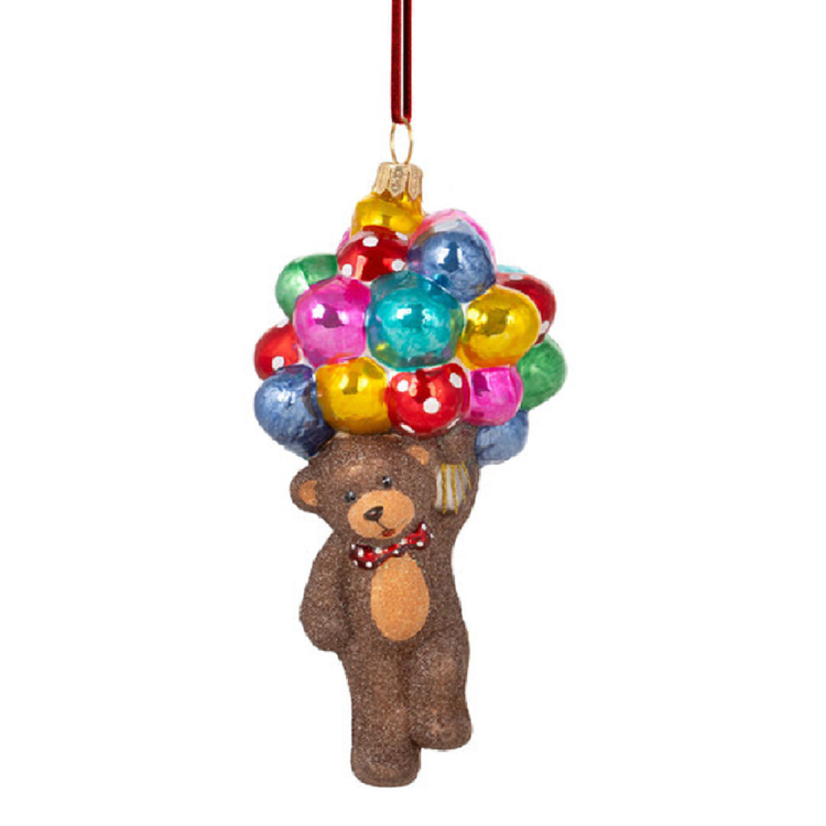 A brown teddy bear Christmas ornament carrying a cluster of colorful balloons in red, yellow, green, blue, pink, and gold, hanging from a red ribbon on a white background.