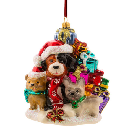 A festive Christmas ornament featuring three dogs dressed in holiday attire, surrounded by colorful wrapped gifts and a red Santa hat, hanging from a red ribbon on a white background.