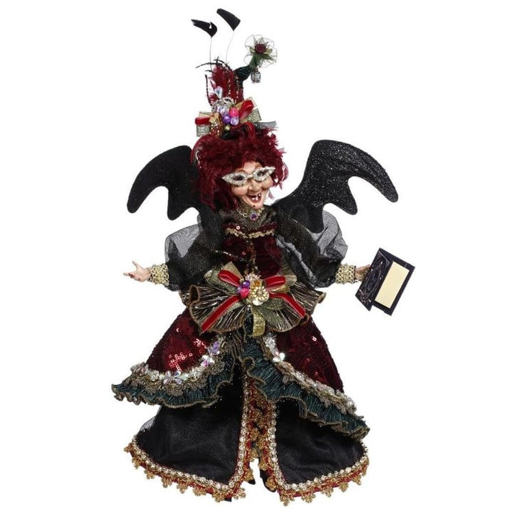 witch figurine with black bat wings, wearing red sequin dress and holding a book of magic.