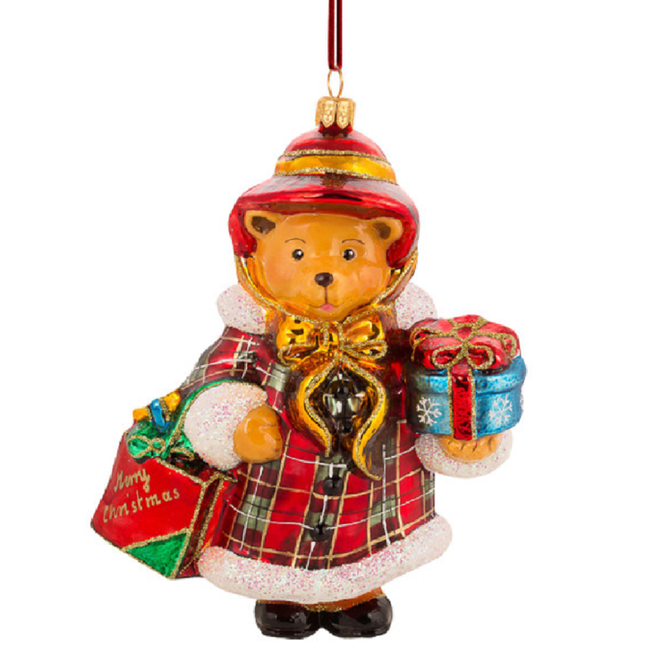 A festive teddy bear Christmas ornament wearing a red and gold plaid coat and matching hat, holding a red gift bag that says 'Merry Christmas' and a blue gift box with a red bow, on a white background.