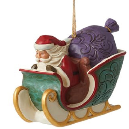 hanging ornament shaped like a sleigh in green with red trim and gold runners. Santa Claus is driving and has a stuffed purple bag in the back.