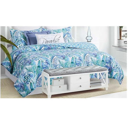 bed made in a quilt with blue and green palm tree and fern print. There are matching pillows on the bed and room furniture to showcase the comforter.