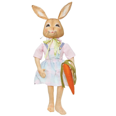 Fabric bunny rabbit figurine, she is wearing a pink shirt with a pink and blue plaid dress and holding a carrot.