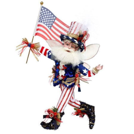 Bearded fairy wearing blue sequined top, red and white stripe pants, a top hat that is red white and blue, and is holding an American Flag