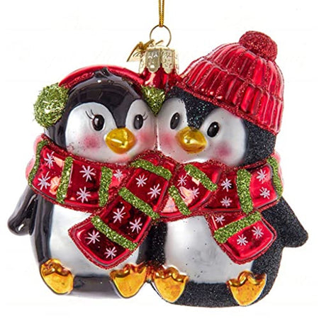 one ornament showing 2 penguins in black and white wearing red scarf and ear muffs and a knit hat 