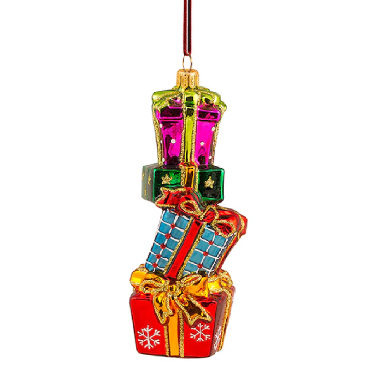 A Christmas ornament shaped like a stack of wrapped presents, with red, blue, green, and gold colors, hanging from a thin red ribbon against a white background.