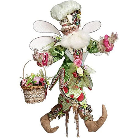 Fairy figurine wearing a white chef type hat and white wings. He carries a basket of flowers and a green vest, watermelon print pants and tan booties.