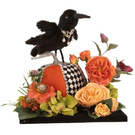 Tablescape featuring a crow standing on a black and orange pumpkin surrounded by pink and orange flowers.