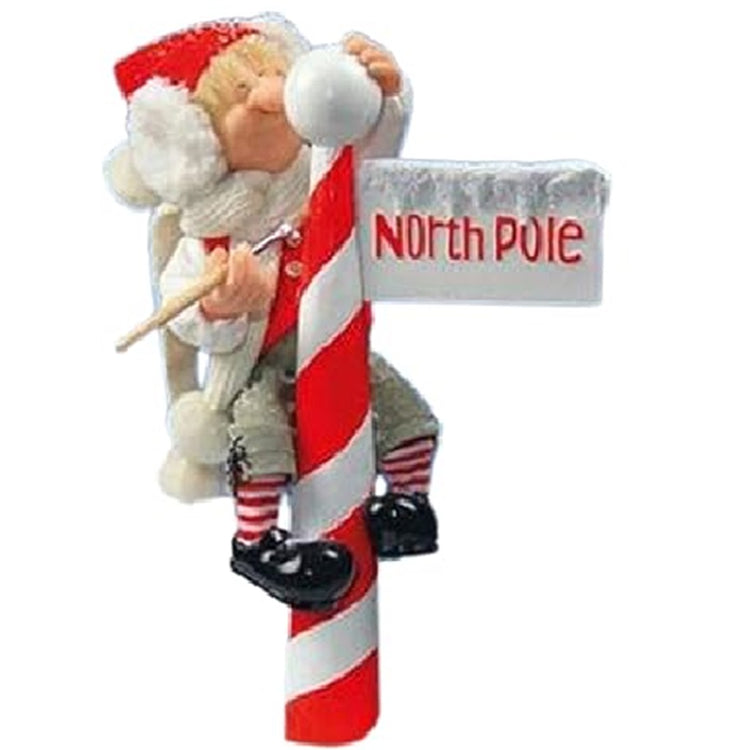 Candy Cane like Pole with a sign that says North Pole. Reggie an elf is climbing the poll to paint a snowball at the top.