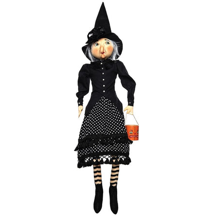 witch figuirne wearing a black top with black and white polka dot skirt and a black witch hat. holding a candy bucket that is painted like a jack o lantern.