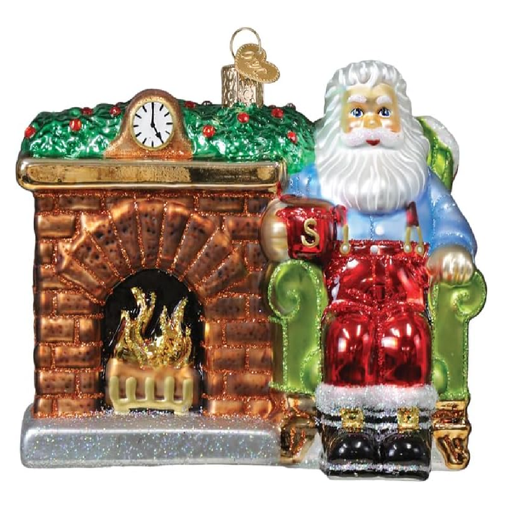 blown glass hanging ornament, santa in a green arm chair next to a lit fireplace.