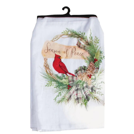 Folded white kitchen towel on hanger with a red cardinal sitting in a wreath and a banner that says season of peace