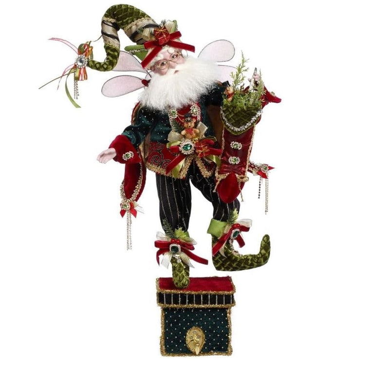 Bearded fairy figurine wearing dark green velvet suit, a green stocking cap and holding a red stocking with pine needles in it. He's standing on a box with a hook for an actual stocking.