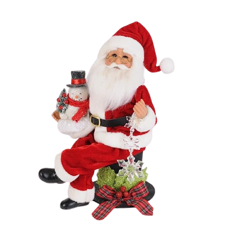 Santa figurine wearing traditional red suit, sitting on a top hat with holly and plaid ribbon detail. He's holding a snowman in one hand and a snowflake ornament in the other.