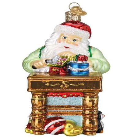 blown glass ornament depicting santa working at his toyshop table.