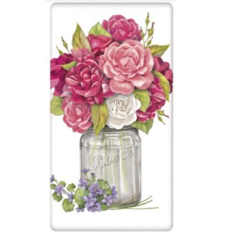 White towel with a clear jar of Roses.  The roses aner shades of pink with 1 white rose.  There is a sprig of purple flowers on the bottom outside of the jar.