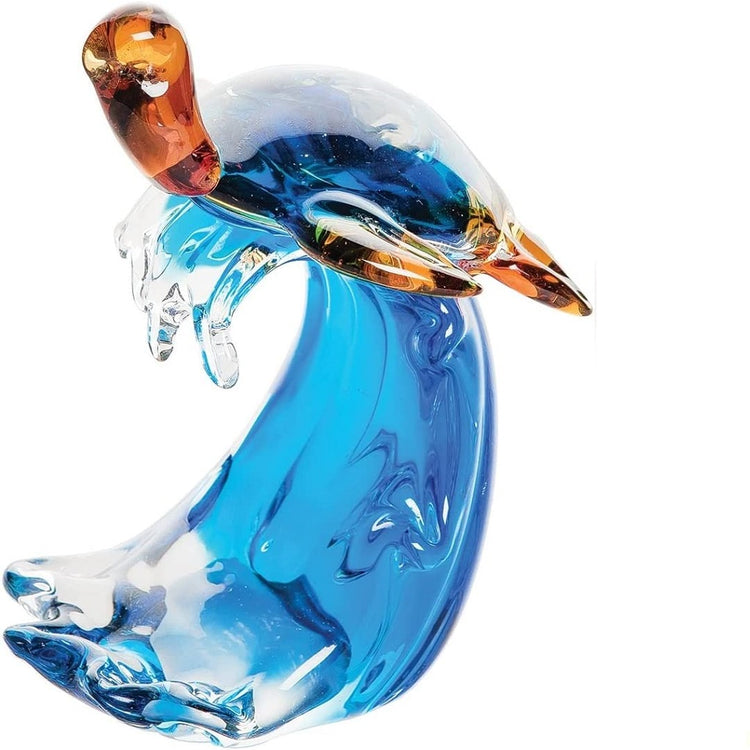 Glass tabletop decorative piece shaped like a turtle riding a wave.  The wave is both clear glass with blue color.  The turtle has a clear shell with blue color under neath and brown fins and head.
