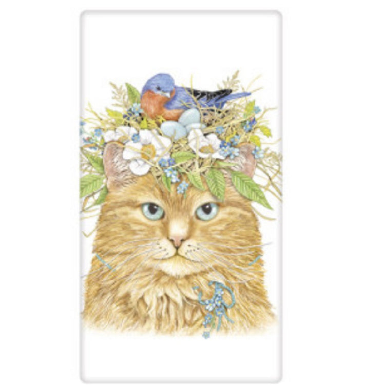 White towel with a calico cat wearing a crown of flowers with a blue bird on top.  Cat wears a blue string collar