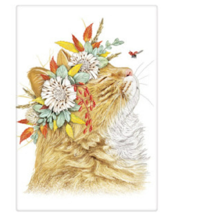 White kitchen towel with a side view of a tan cat. The cat has their eyes closed and they are looking up at a bee. Cat is wearing a crown of white flowers and leaves