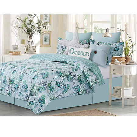 Shorecrest quilt set shown on a bed, the quilt and matching pillow shams are a light blue with green and teal coral, shell, and jellyfish pattern.