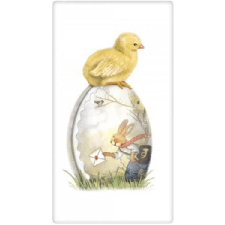 Yellow chick sitting on top of an Easter egg lying in the grass. The egg has a picture of a bunny delivering mail.