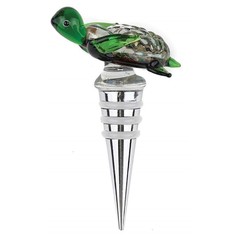 Clear Green glass turtle sitting on top of silver bottle stopper. Turtle shell is brown.